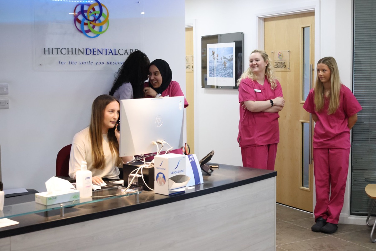 The reception at Hitchin Dental Care, with the practice logo on the wall and the team at the front desk