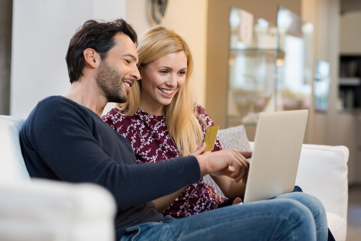 A couple sitting on a sofa looking at a laptop together, one of them holding a bank card